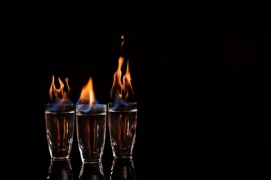 Photo of Flaming vodka in shot glasses on black background, space for text