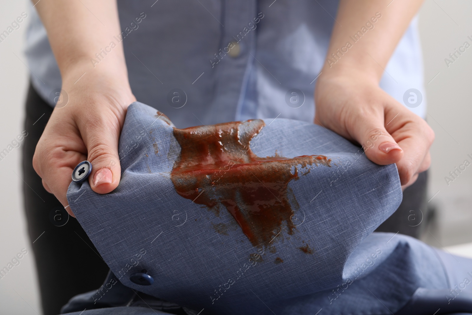 Photo of Woman holding shirt with stain of sauce on blurred background, closeup