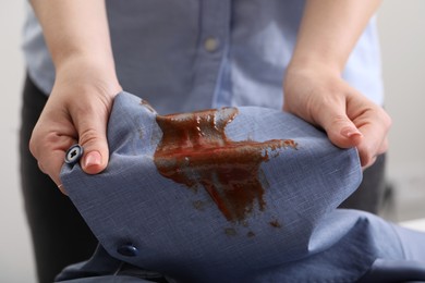 Woman holding shirt with stain of sauce on blurred background, closeup