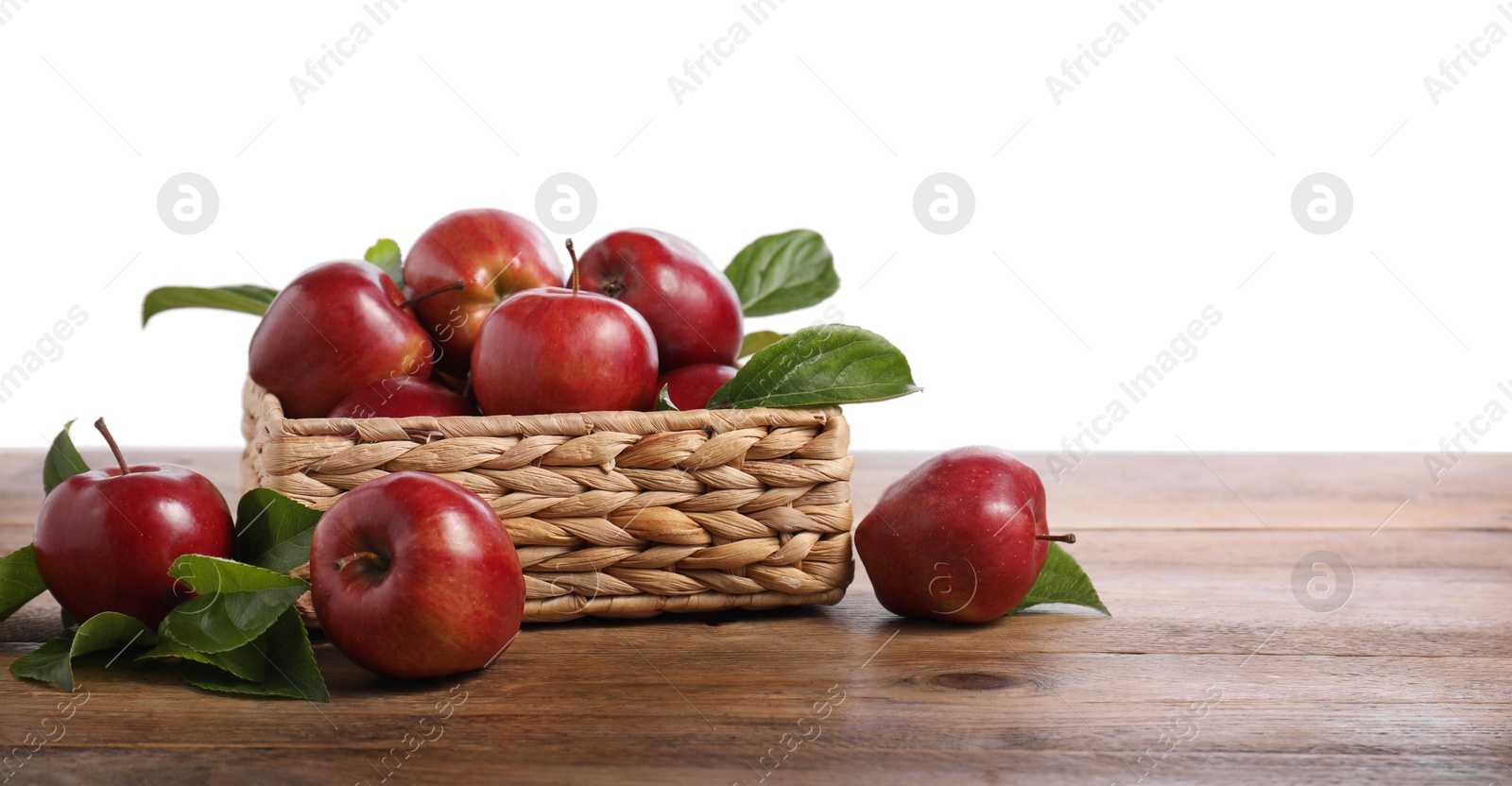 Photo of Fresh red apples and leaves in basket on wooden table against white background. Space for text