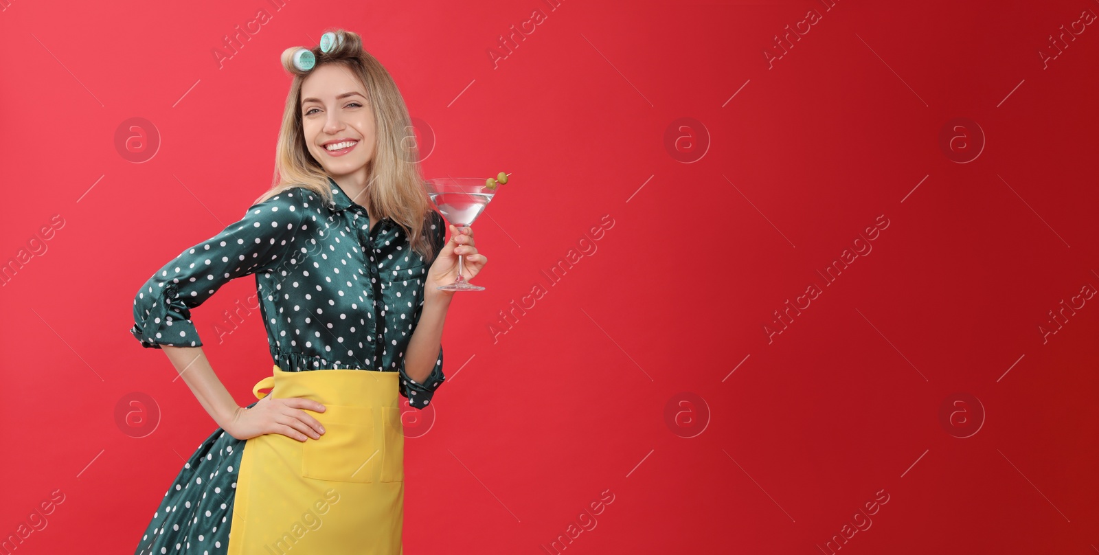 Photo of Young housewife with glass of martini on red background. Space for text