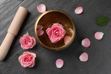 Photo of Tibetan singing bowl with water, beautiful rose flowers and mallet on gray table, flat lay