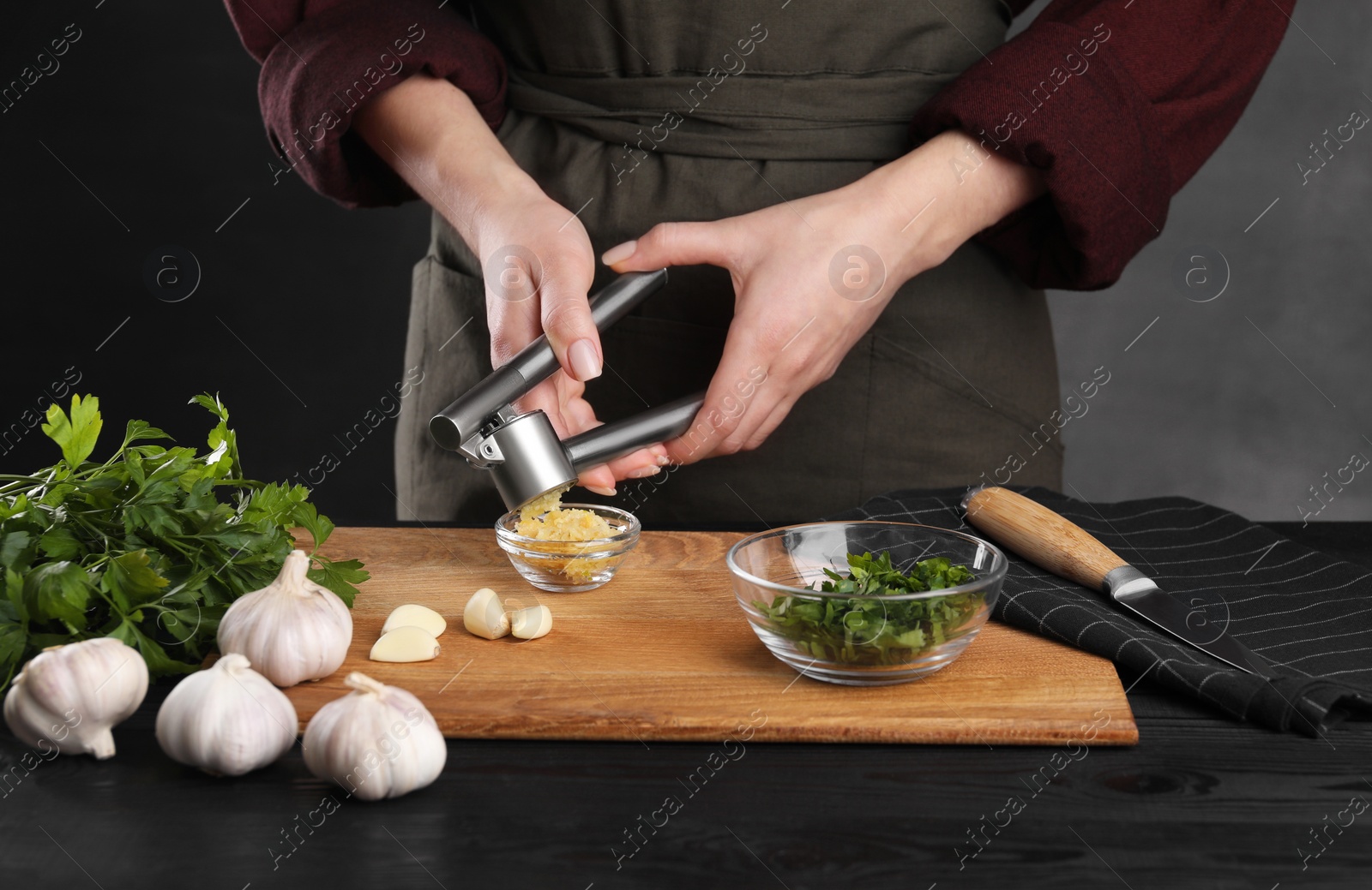 Photo of Woman squeezing garlic with press at black wooden table, closeup