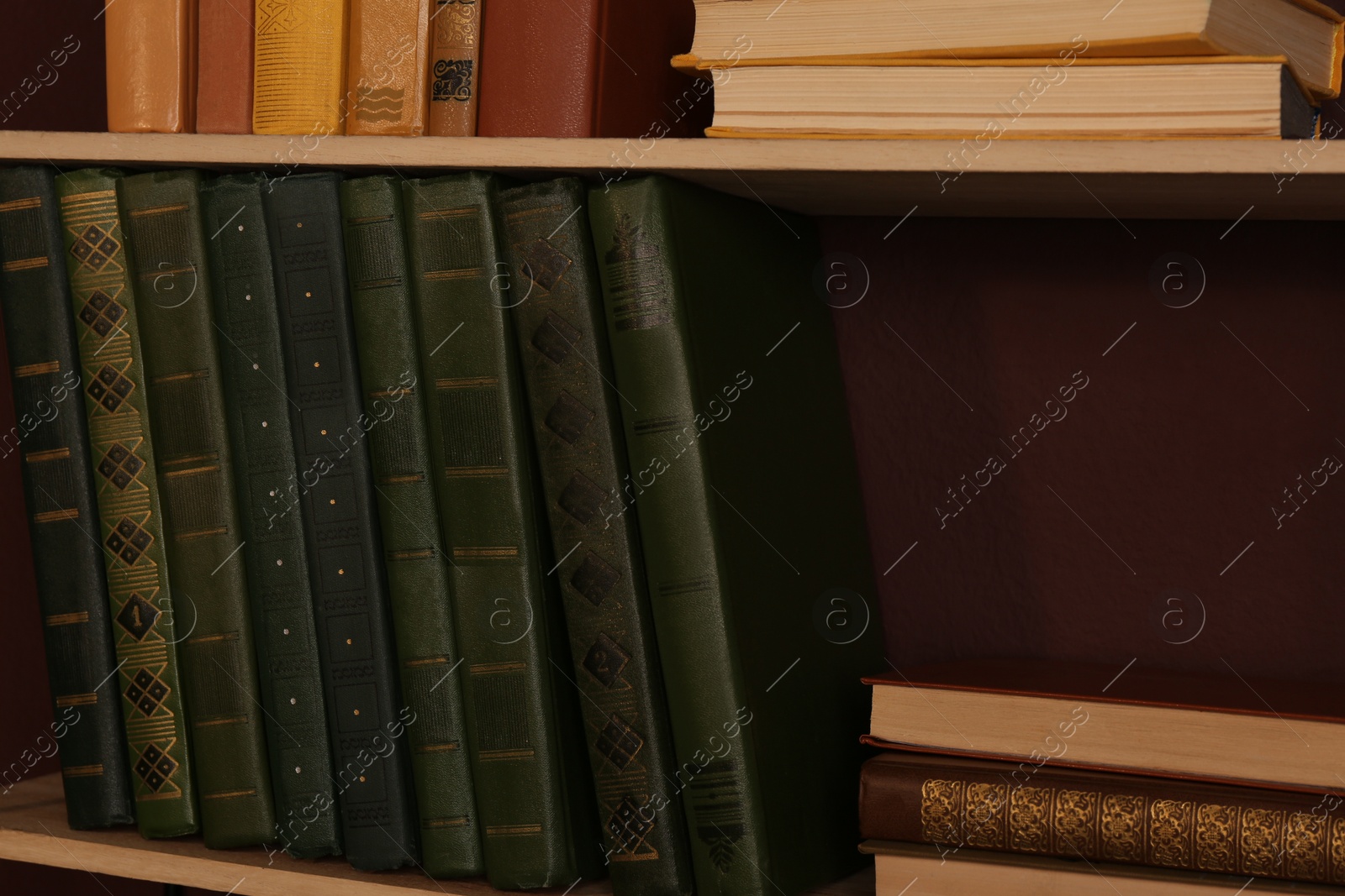 Photo of Shelves with different books on brown wall, closeup