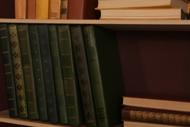 Shelves with different books on brown wall, closeup