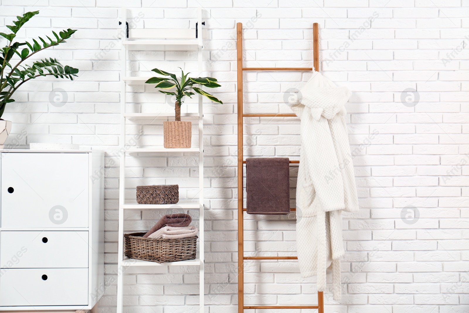 Photo of Furniture with clean towels and robe near brick wall in bathroom