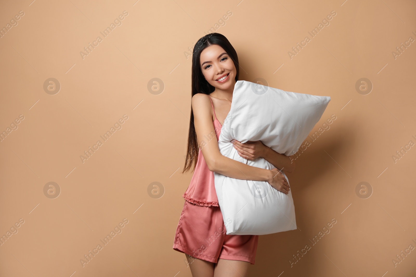 Photo of Beautiful Asian woman with pillow on beige background. Bedtime