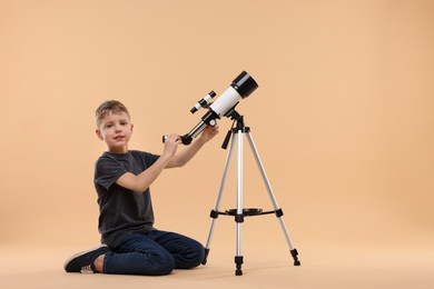 Cute little boy with telescope on beige background, space for text