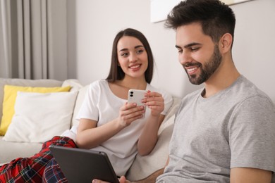 Photo of Happy couple in pajamas with gadgets on sofa at home