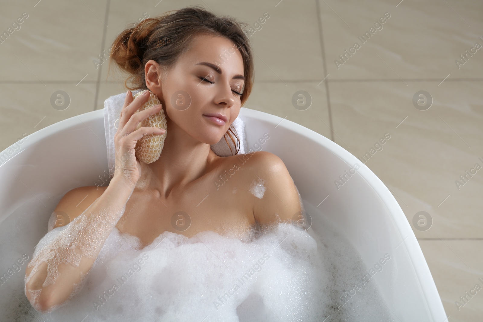 Photo of Beautiful woman with sponge taking bath indoors