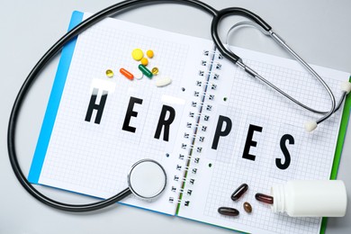 Photo of Notebook with word Herpes, different pills and stethoscope on grey background, flat lay