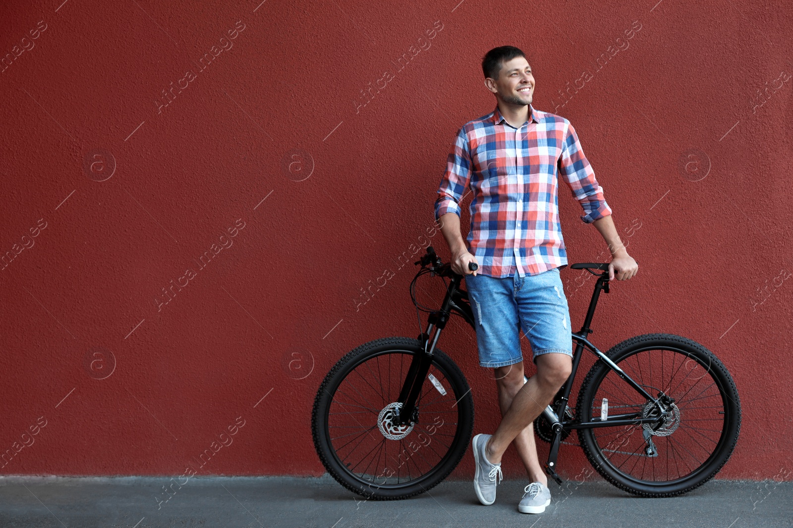 Photo of Handsome man with modern bicycle near red wall outdoors