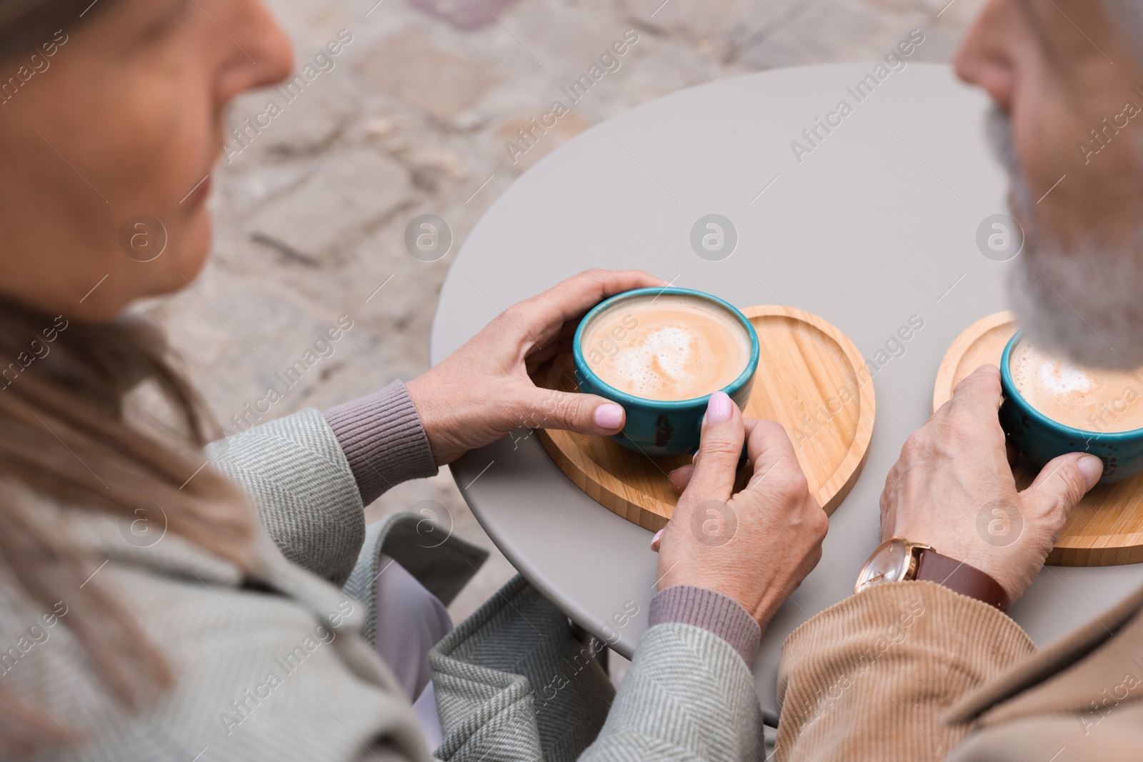 Photo of Affectionate senior couple with coffee at table outdoors, closeup