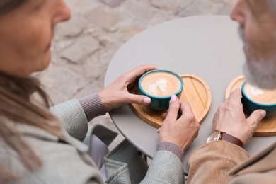Photo of Affectionate senior couple with coffee at table outdoors, closeup