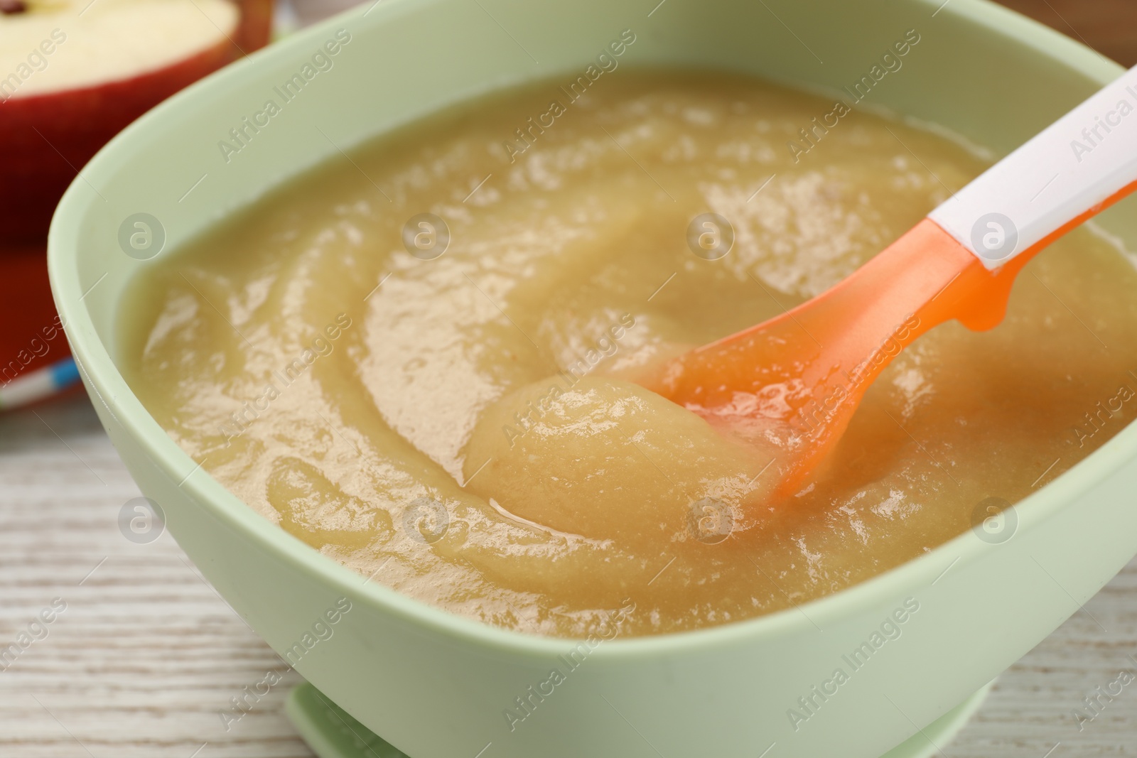 Photo of Healthy baby food. Bowl with delicious apple puree on white wooden table, closeup