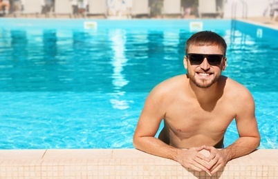 Young bearded man in swimming pool at resort. Space for text