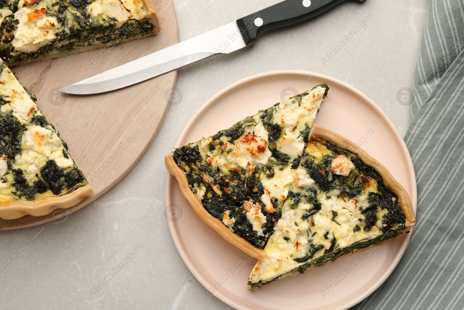 Photo of Pieces of delicious homemade spinach quiche and knife on light table, flat lay
