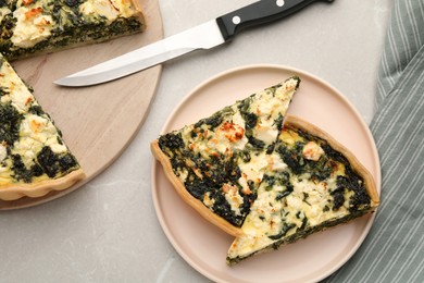Pieces of delicious homemade spinach quiche and knife on light table, flat lay