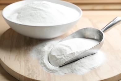 Photo of Baking soda in scoop and bowl on wooden table