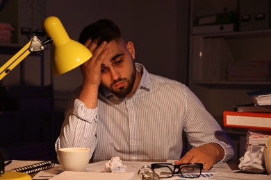 Photo of Overwhelmed man at workplace in office at night