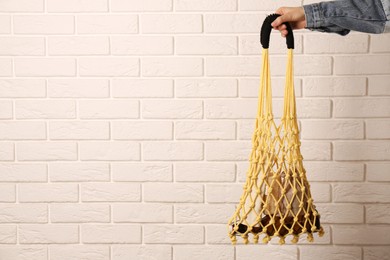 Photo of Woman holding net bag with different items against brick wall, closeup and space for text. Conscious consumption