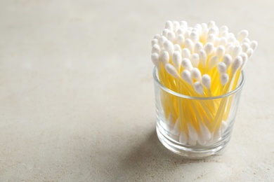 Glass with cotton swabs on grey background. Space for text