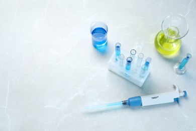 Laboratory analysis. Micropipette and different glassware with liquids on light grey marble table, above view. Space for text