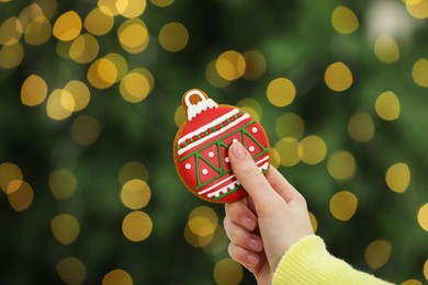 Photo of Woman with decorated cookie against blurred Christmas lights, closeup