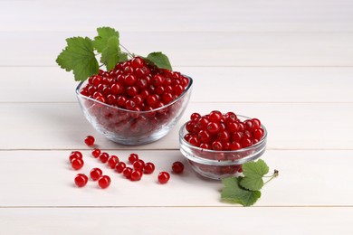 Many ripe red currants and leaves on white wooden table