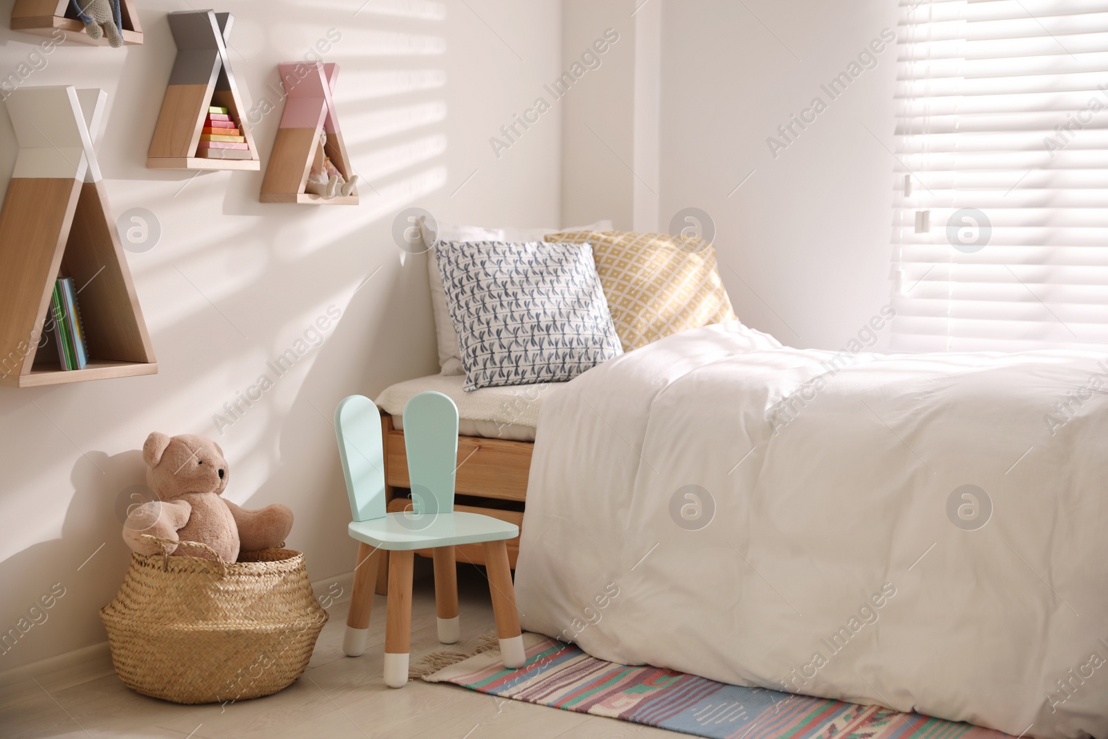 Photo of Cute little chair with bunny ears near bed indoors. Children's room interior