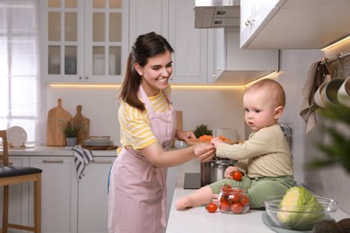 Photo of Happy young woman with her cute baby spending time together in kitchen