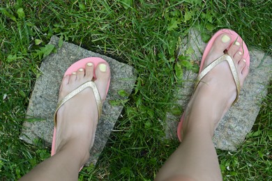 Woman wearing stylish flip flops on green grass outdoors, top view