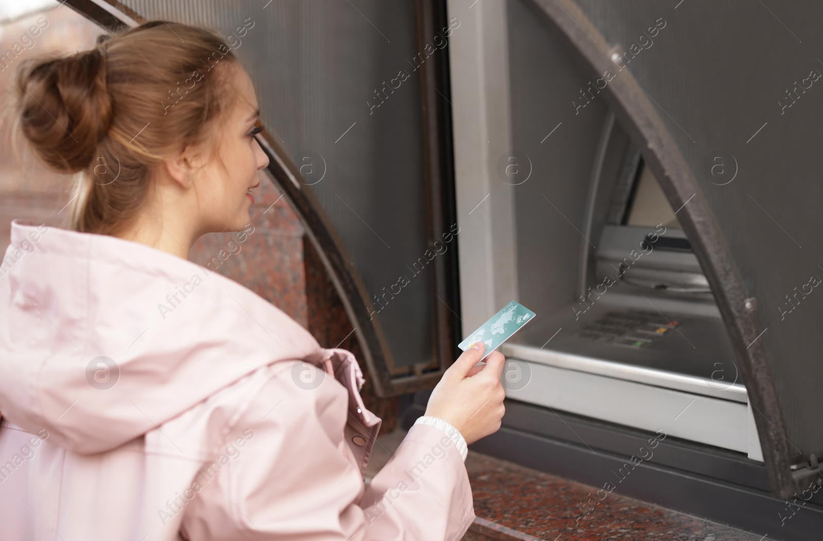 Photo of Young woman with credit card using cash machine outdoors