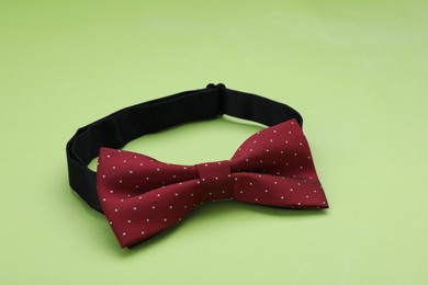 Photo of Stylish burgundy bow tie with polka dot pattern on light green background