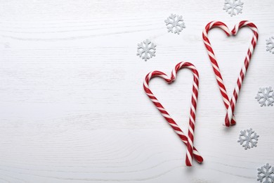 Photo of Hearts made of sweet Christmas candy canes and snowflakes on white wooden table, flat lay. Space for text