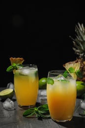 Glass of delicious cocktail decorated with ice and mint on grey table against black background