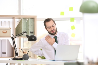 Photo of Young man suffering from shoulder pain in office