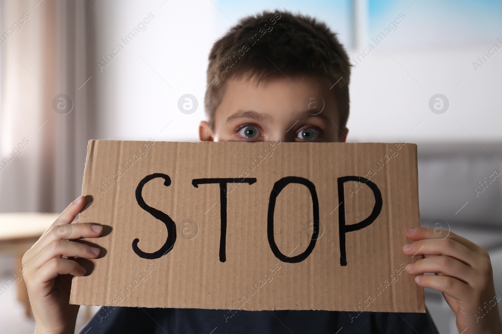 Photo of Abused little boy with sign STOP indoors. Domestic violence concept