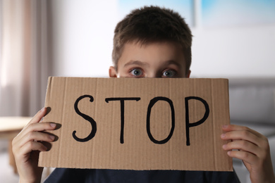 Abused little boy with sign STOP indoors. Domestic violence concept