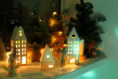Photo of Christmas atmosphere. Beautiful glowing houses, fir trees and toys on window sill indoors