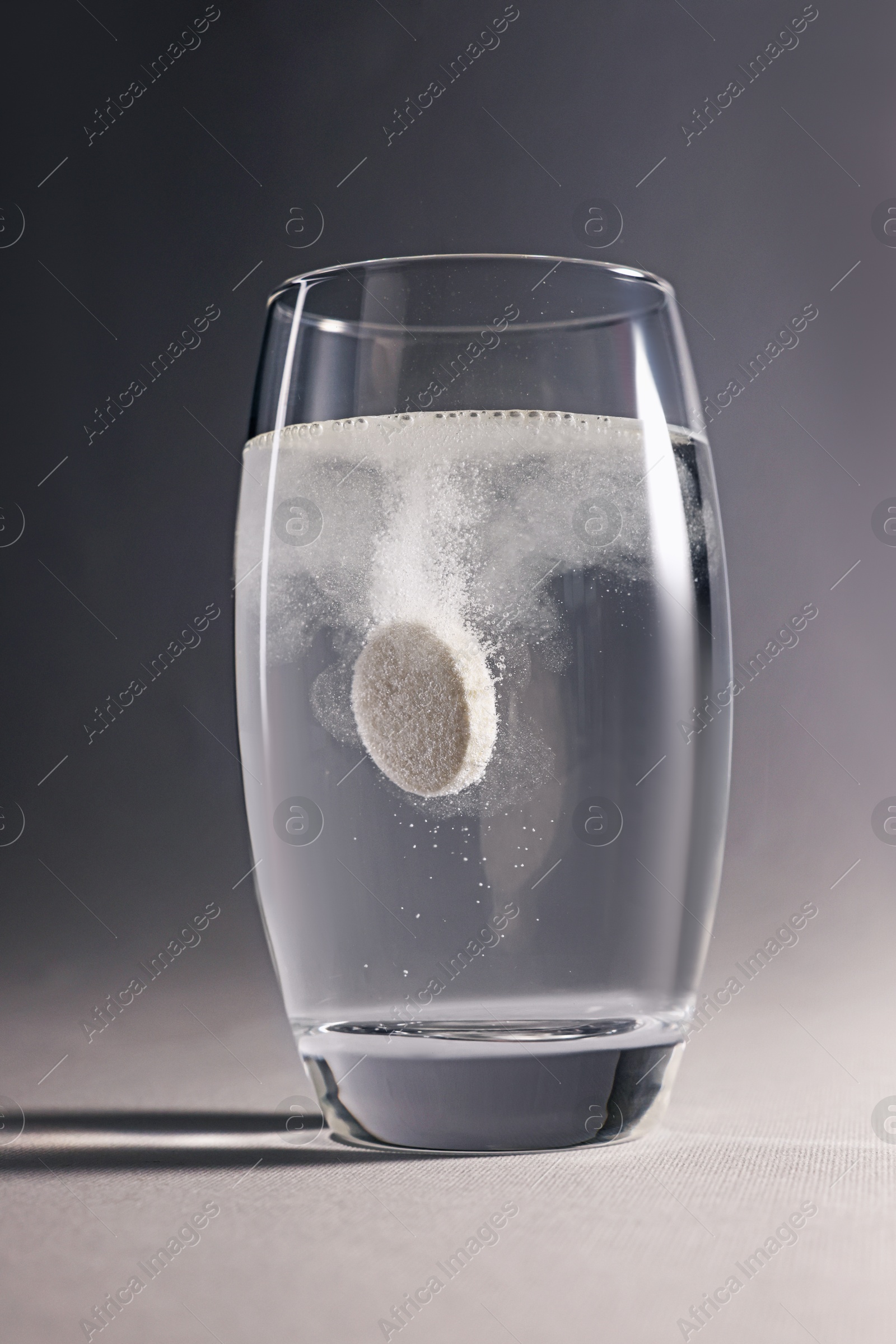 Photo of Effervescent pill dissolving in glass of water on grey background