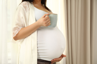 Photo of Pregnant woman with cup of hot drink at home, closeup