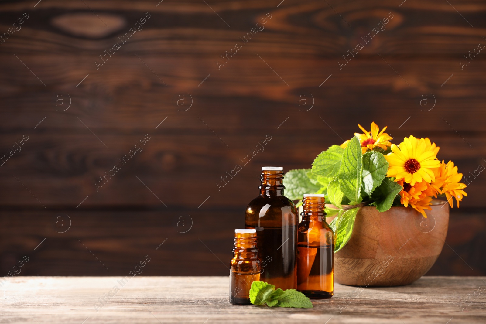 Photo of Bottles with essential oils, mint and flowers on wooden table. Space for text