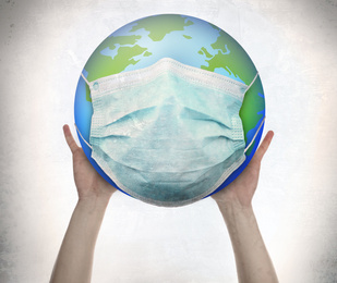 Man holding Earth with medical mask on white background, closeup. Concept of coronavirus outbreak