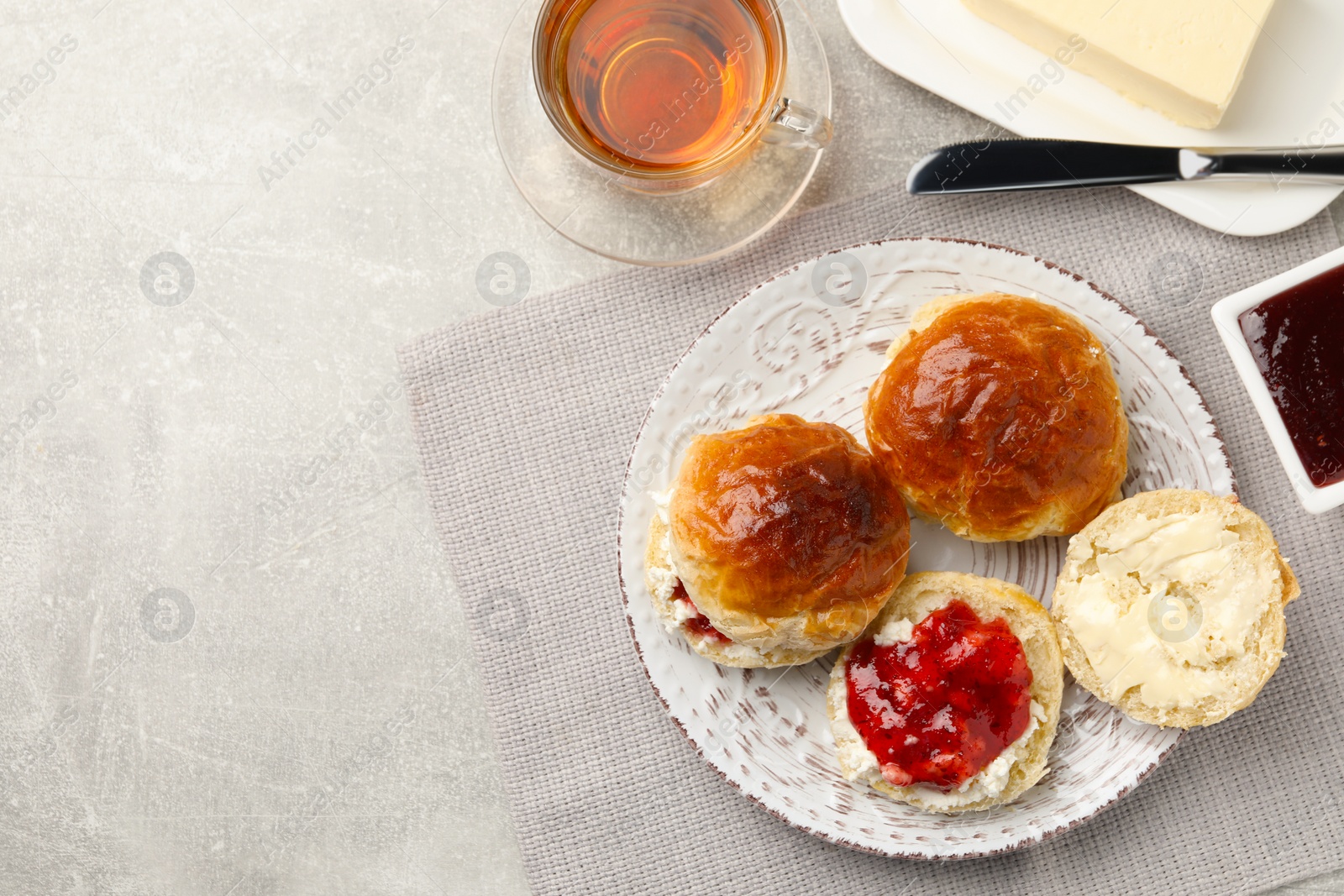 Photo of Freshly baked soda water scones with cranberry jam, butter and cup of tea on light grey table, flat lay. Space for text