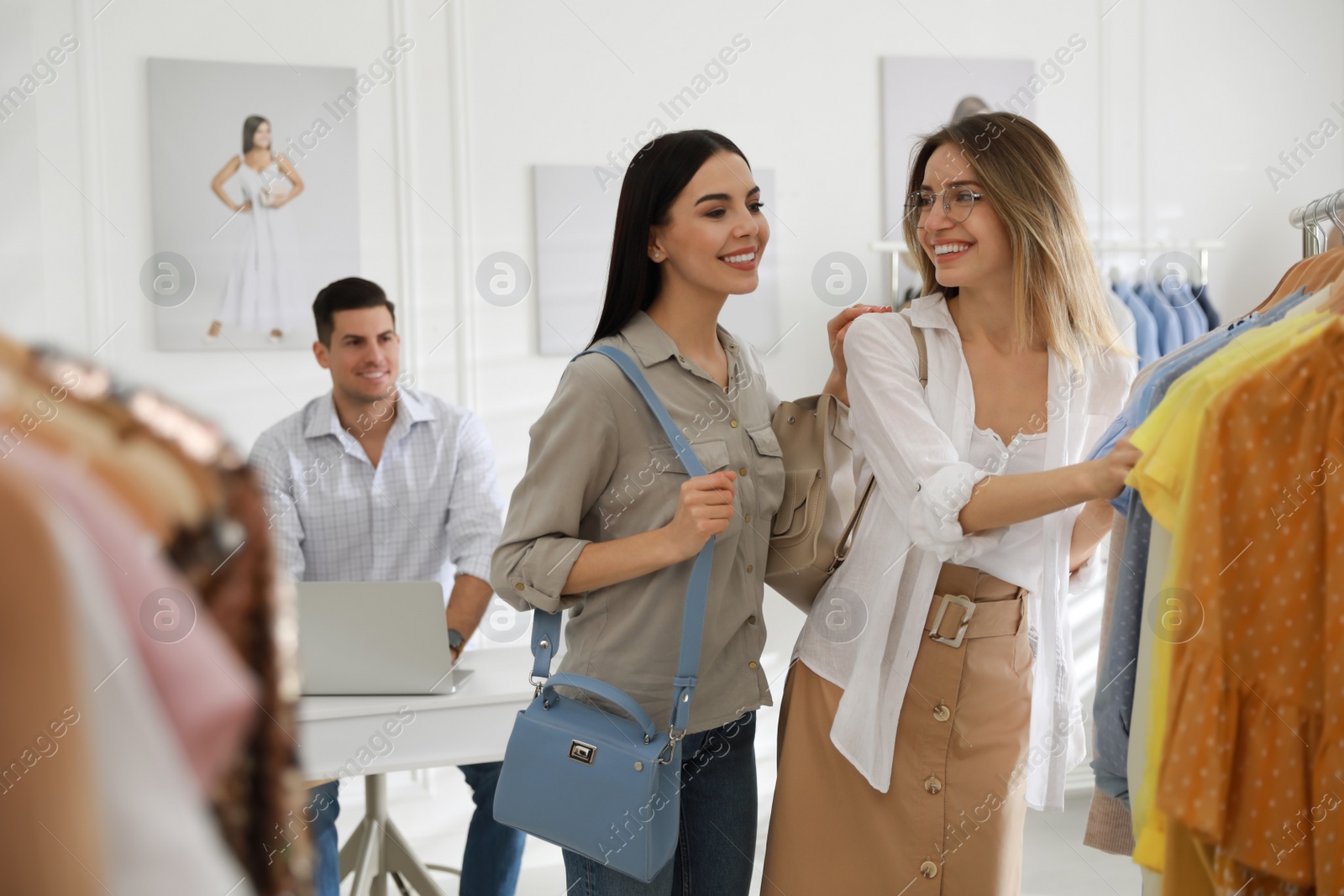 Photo of Young women choosing clothes near rack in modern boutique