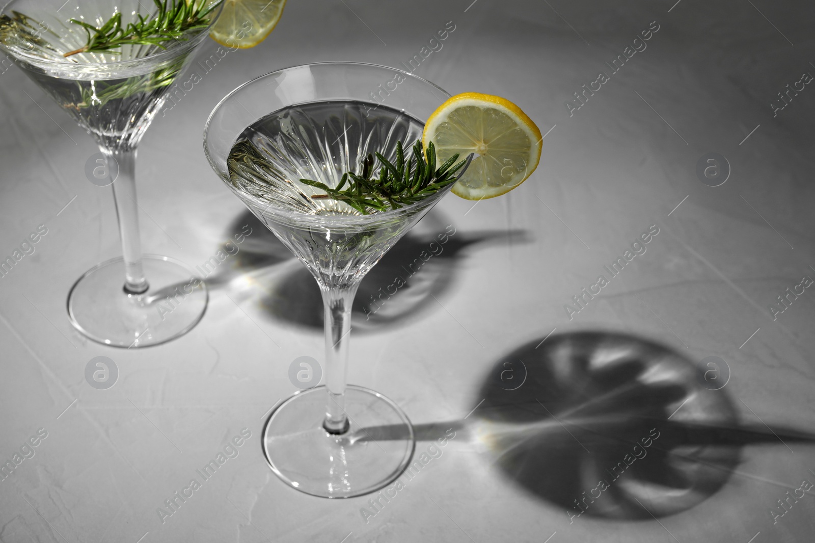 Photo of Martini glasses of refreshing cocktail decorated with lemon slices and rosemary on grey textured table. Space for text