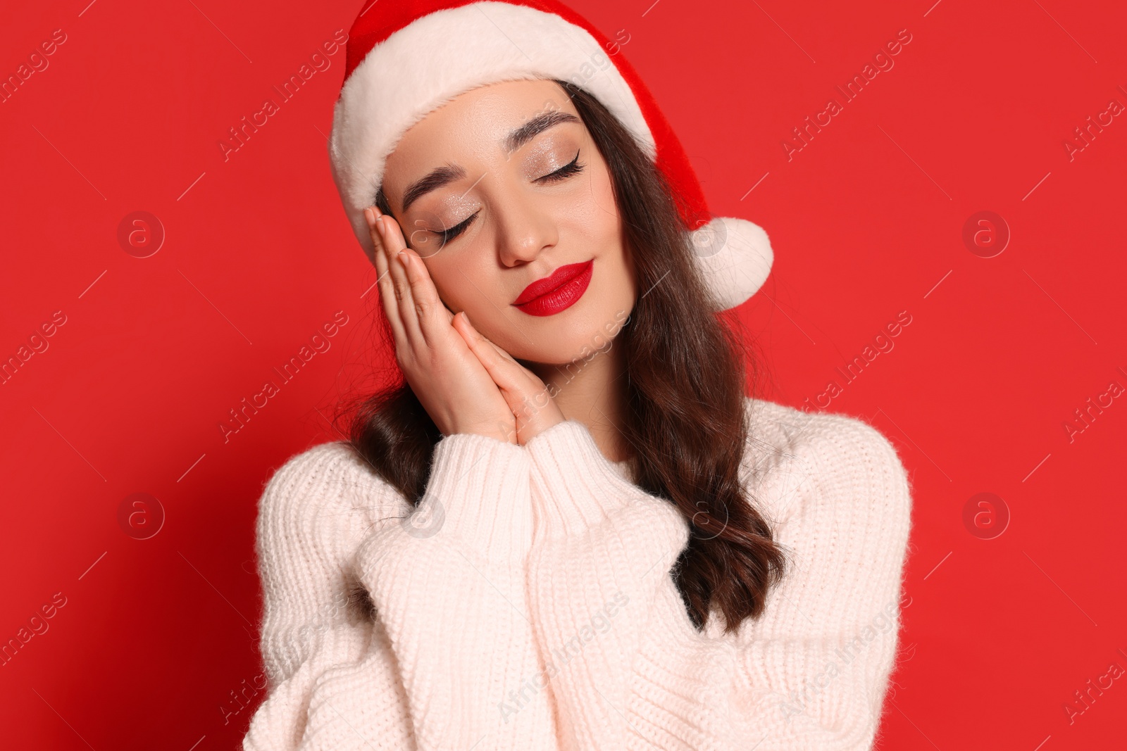 Photo of Christmas celebration. Beautiful young woman in Santa hat on red background