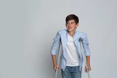 Photo of Teenage boy with injured leg using crutches on grey background, space for text
