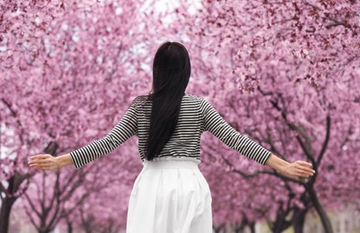 Photo of Young woman in park with blooming trees. Spring look